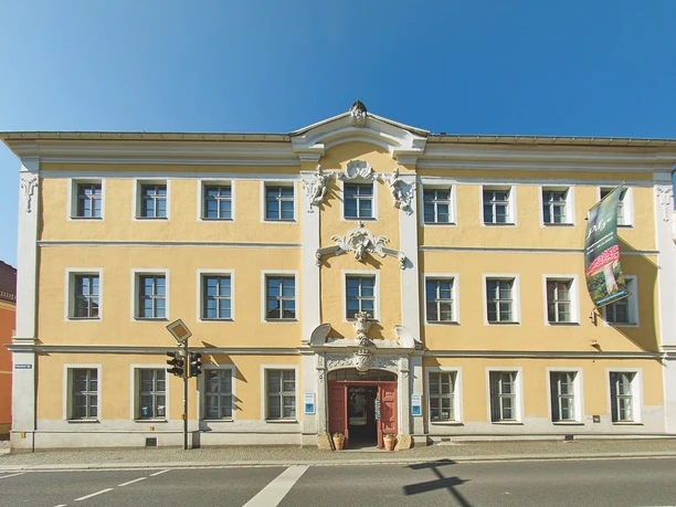 Museum Außenansicht Gelbes Barockgebäude mit weißer Verzierung, 5-bogige Fensterfront, doppelte Eingangstür.