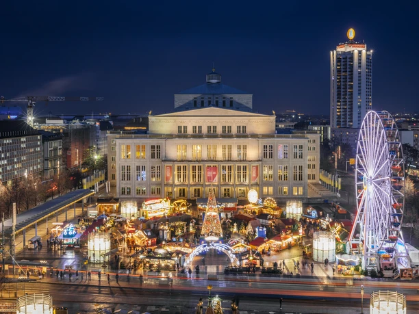 View of the brightly lit Augustusplatz with the fairytale forest and Ferris wheel in the evening with the opera in the background