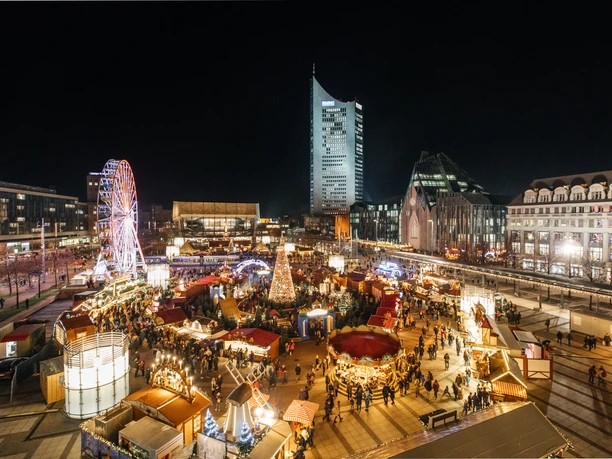 View of the brightly lit Augustusplatz with the fairytale forest and Ferris wheel in the evening with the Gewandhaus and city skyscraper in the background