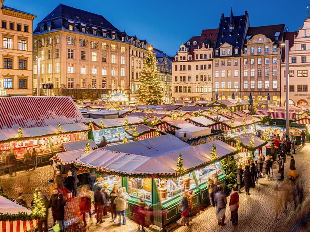 View of the stalls at the brightly lit Christmas market on the market square in Leipzig in the evening with the large, decorated Christmas tree