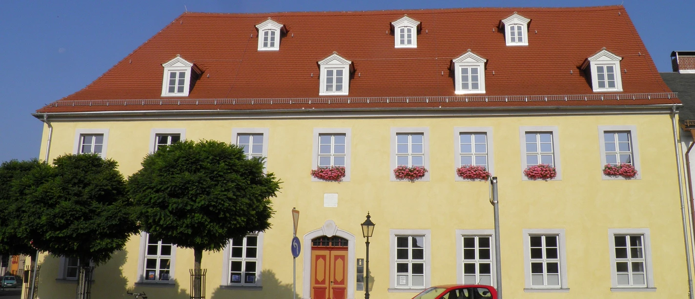 Infopoint und Bibliothek im Napoleonhaus Pegau Das Bild zeigt die gelbe Front des Napoleonhauses, welche unter anderem die Tourist-Information beherbegt.