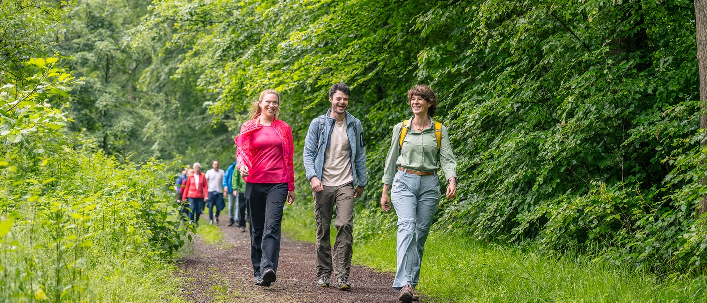 Eröffnungswanderung mit Landrätin Dr. Bettina Warnecke Freunde spazieren auf einem Waldweg in Ratingen, umgeben von üppigem Grün und dichtem Laubwerk.