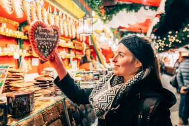 A woman stands in front of a gingerbread stall at Leipzig's Christmas market and reaches for a gingerbread heart