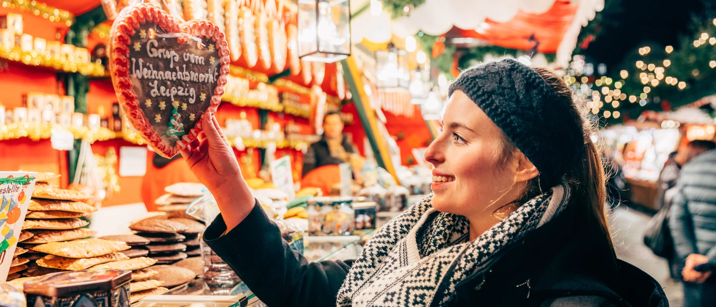 A woman stands in front of a gingerbread stall at Leipzig's Christmas market and reaches for a gingerbread heart