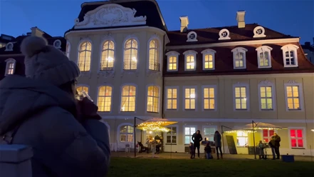 Weihnachtsduft und Lichterglanz am Gohliser Schlösschen - Weihnachten in Leipzig Eine Frau blickt mit Heißgetränk in der Hand auf das erleuchtete Gohliser Schlösschen am Abend