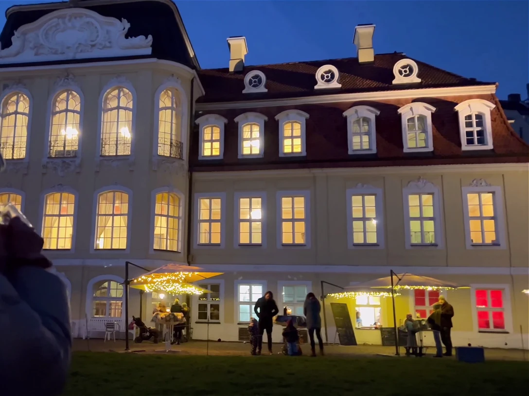 Weihnachtsduft und Lichterglanz am Gohliser Schlösschen - Weihnachten in Leipzig Eine Frau blickt mit Heißgetränk in der Hand auf das erleuchtete Gohliser Schlösschen am Abend