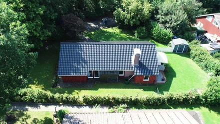 Ferienpark Extertal_Ferienhaus Elch.jpg Ferienhaus mit schwarzem Dach umgeben von grüner Landschaft und Bäumen; helle Terrasse hinten.