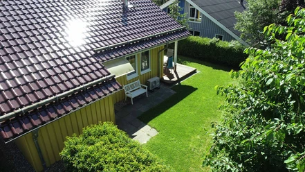 Ferienpark Extertal_Haus Alissa Gelbes Ferienhaus mit rotem Ziegeldach, Veranda, Gartenbank und umgeben von viel Grün.