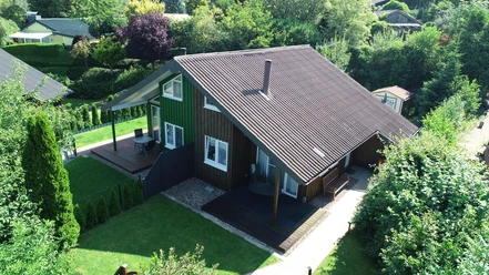 Ferienpark Extertal_Haus Blaumeise Zweistöckiges, braunes Holzferienhaus mit großer Terrasse, umgeben von grüner, bewaldeter Natur.