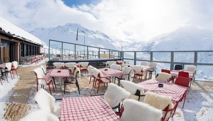 Sonnige Terrasse der NätschenArena mit Tischen, Fellen und Blick auf verschneite BergeSnow-covered terrace of Bergrestaurant NätschenArena with mountain panorama and checked tables