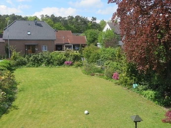 Suedzimmer-Ausblick Ein gepflegter Garten mit grünem Rasen, Blumenbeeten, einem Fußball; Häuser im Hintergrund.