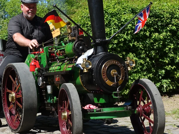 Dampftraktor Ein Mann steht neben einem grünen Miniatur-Dampftraktor mit deutschen und britischen Flaggen.