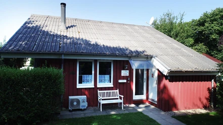 Ferienpark Extertal_Haus Merle Rotes Ferienhaus mit schrägem Dach, weißen Fensterrahmen und Eingangstür, umgeben von Grün.