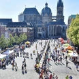 Lange Tafel der Vielfalt_51.jpg Blick auf den Aachener Dom und den Katschhof, auf dem zwei Stände und viele Tische, an denen Personen sitzen oder stehen, aneinander gereiht sind.