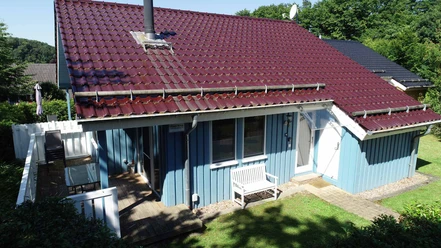 Ferienpark Extertal_Haus Nina Ferienhaus mit rotem Ziegeldach, blauen Holzfassaden und kleiner Holzterrasse im Grünen umgeben.