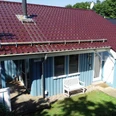 Ferienpark Extertal_Haus Nina Ferienhaus mit rotem Ziegeldach, blauen Holzfassaden und kleiner Holzterrasse im Grünen umgeben.