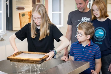 kreatives Papierschöpfen Junge besucht mit Familie eine Ausstellung. Kind schöpft Papier. Andere schauen interessiert zu.