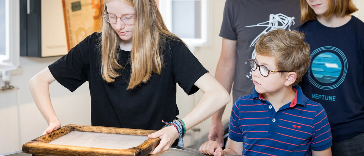 kreatives Papierschöpfen Junge besucht mit Familie eine Ausstellung. Kind schöpft Papier. Andere schauen interessiert zu.
