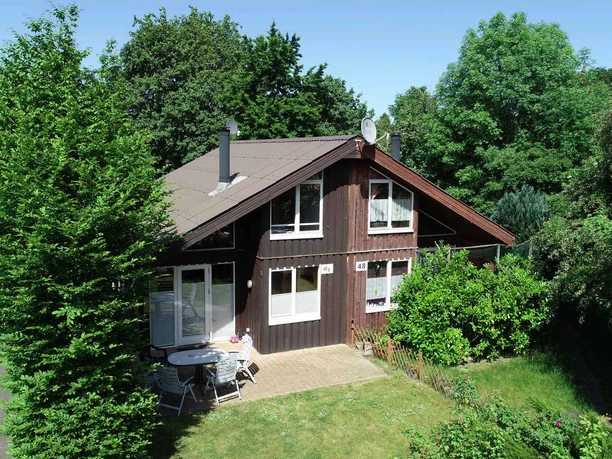 Ferienpark Extertal_Ferienhaus Lene Ein Ferienhaus mit Holzwänden, umgeben von üppigem Grün, mit Terrasse und Gartenmöbeln.