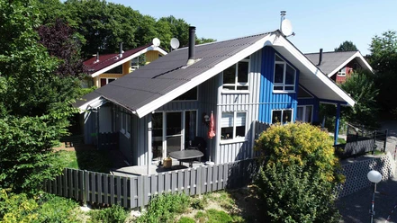 Ferienpark Extertal_Haus Weitblick Ein modernes Ferienhaus mit blau-grauer Fassade und umliegendem Garten in einer bewaldeten Gegend.