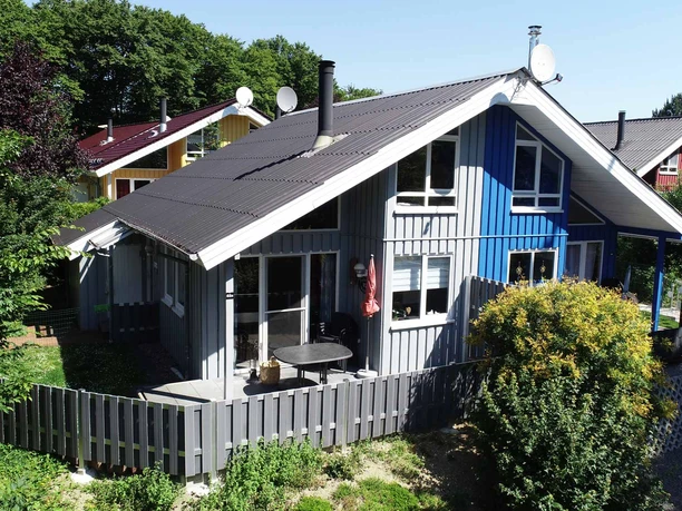 Ferienpark Extertal_Haus Weitblick Ein modernes Ferienhaus mit blau-grauer Fassade und umliegendem Garten in einer bewaldeten Gegend.