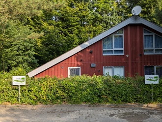 Ferienpark Extertal_Premium-Ferienhaus Rot Premium-Ferienhaus in roter Farbe zwischen dichtem Grün, mit Sat-Schüssel und gepflastertem Weg.