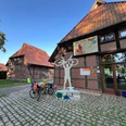 Skulptur eines Radfahrers mit erhobenem Fahrrad vor einem Fachwerkgebäude mit Fahrradständer.