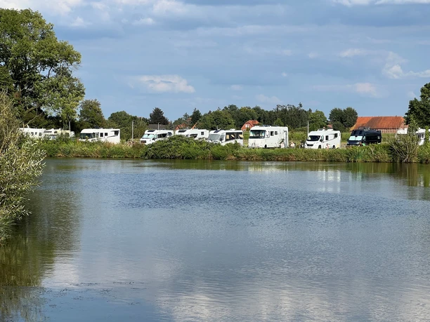 Wohnmobile stehen entlang eines gewundenen Flusses, umgeben von üppigem Grün und strahlendem Himmel.