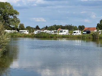 Womo Landesbergen Wohnmobile stehen entlang eines gewundenen Flusses, umgeben von üppigem Grün und strahlendem Himmel.
