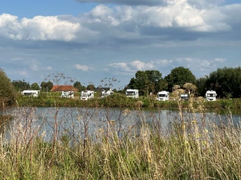 Wohnmobile parken entlang eines Sees, umgeben von Natur und wolkigem Himmel in Landesbergen.