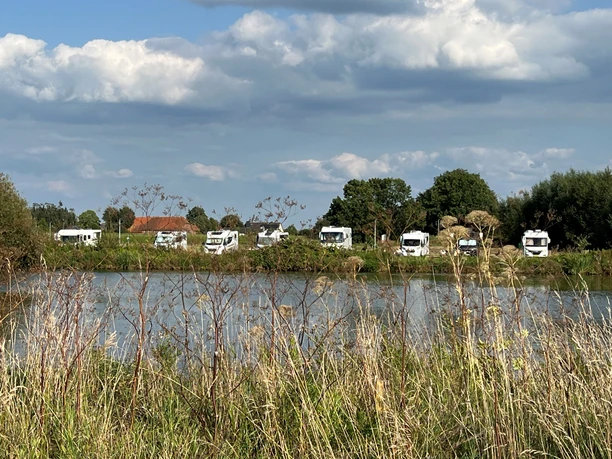 Wohnmobile parken entlang eines Sees, umgeben von Natur und wolkigem Himmel in Landesbergen.
