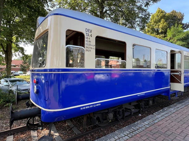 A blue, vintage train car stands on a section of track, with trees in the background.