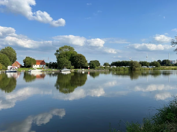 Wassersportverein Landesbergen Der Wassersportverein in Landesbergen spiegelt sich in einem ruhigen Fluss, umgeben von grüner Natur.