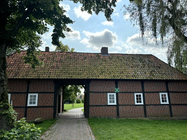 Torhaus am Bürgerpark ©Emsland Tourismus GmbH Backstein-Torhaus mit rotem Ziegeldach, von Bäumen umgeben, führt auf gepflastertem Weg in den Park.