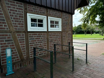 Torhaus am Bürgerpark ©Emsland Tourismus GmbH Rotes Fachwerkgebäude mit zwei weißen Fenstern, daneben Fahrradständer und grüne Parkfläche.