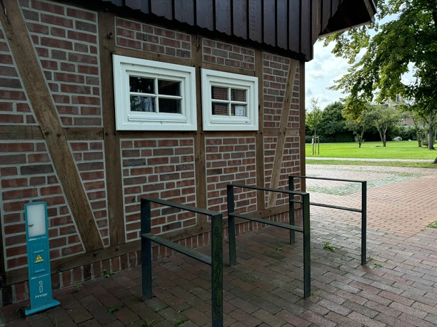 Torhaus am Bürgerpark ©Emsland Tourismus GmbH Rotes Fachwerkgebäude mit zwei weißen Fenstern, daneben Fahrradständer und grüne Parkfläche.