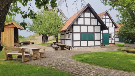 Windmühle Südhemmern Fachwerkhäuser und Windmühle mit gepflastertem Vorplatz, umgeben von Bäumen und Sitzgelegenheiten.