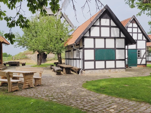 Windmühle Südhemmern Fachwerkhäuser und Windmühle mit gepflastertem Vorplatz, umgeben von Bäumen und Sitzgelegenheiten.