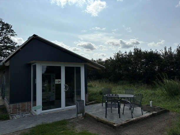 Knues Regiomat ©Emsland Tourismus GmbH Kleines Verkaufsgebäude mit Glasfront, davor Sitzplatz mit Metalltisch und vier Stühlen im Grünen