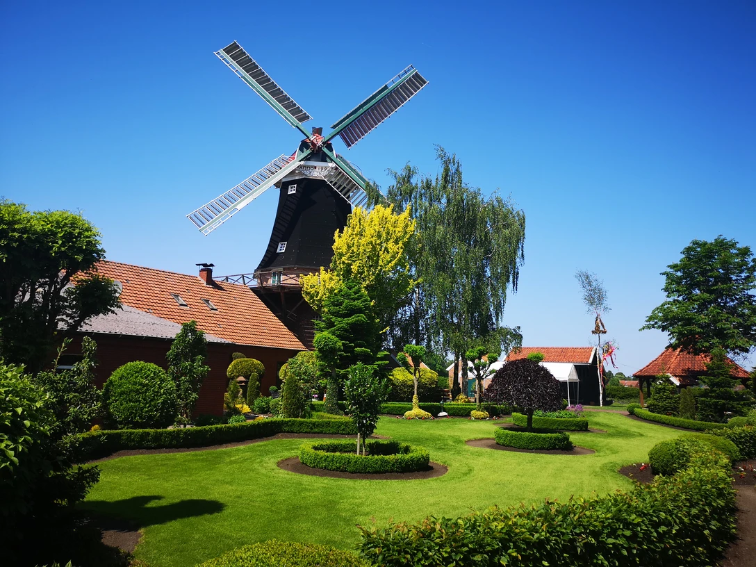 Mühle Rhaude, Rhauderfehn Historische Windmühle mit gepflegtem Garten, rotem Backsteingebäude und blauem Himmel in Rhauderfehn
