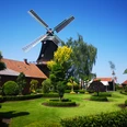 Mühle Rhaude, Rhauderfehn Historische Windmühle mit gepflegtem Garten, rotem Backsteingebäude und blauem Himmel in Rhauderfehn