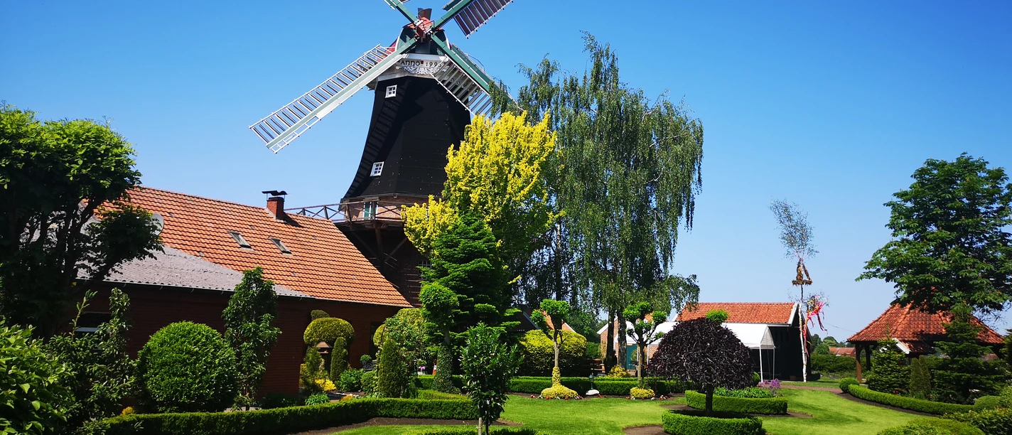 Mühle Rhaude, Rhauderfehn Historische Windmühle mit gepflegtem Garten, rotem Backsteingebäude und blauem Himmel in Rhauderfehn