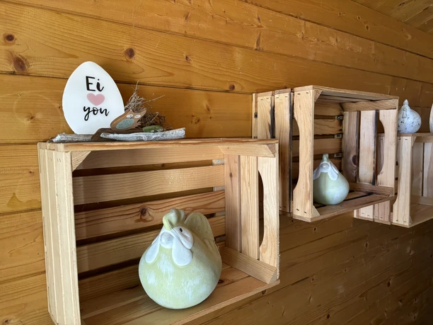 Holzkisten an einer Wand mit Keramikhühnern und einem Ei mit der Aufschrift „Ei love you“.