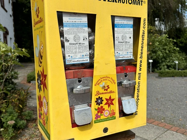 Bibelgarten Lünne ©Emsland Tourismus GmbH Gelber Automat für Bienensaatgut mit Münzeinwurf, aufgestellt im grünen Außenbereich eines Gartens.