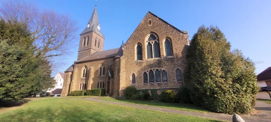 Die Backsteinkirche Schnathorst mit spitzem Turm steht in einer grünen Umgebung unter klarem Himmel.