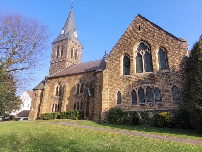 Die Backsteinkirche Schnathorst mit spitzem Turm steht in einer grünen Umgebung unter klarem Himmel.