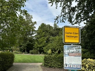 Bibelgarten Salzbergen ©Emsland Tourismus GmbH Eingang zum Bibelgarten Salzbergen mit gelbem Ortsschild und grünem Gartenbereich im Hintergrund.