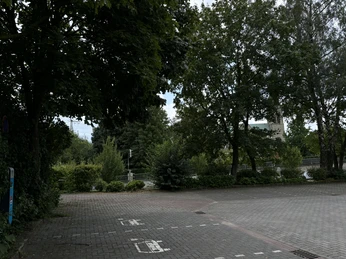 Stellplatz Parkplatz Ortskern ©Emsland Tourismus GmbH Pflasterparkplatz mit Wohnmobilstellflächen, umgeben von Bäumen nahe einer Kirche im Ortszentrum.