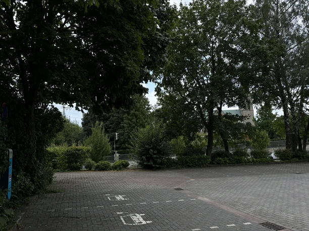 Stellplatz Parkplatz Ortskern ©Emsland Tourismus GmbH Pflasterparkplatz mit Wohnmobilstellflächen, umgeben von Bäumen nahe einer Kirche im Ortszentrum.