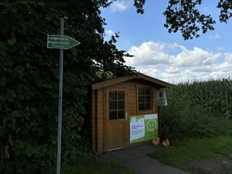 Eierhütte Langenhorst Kleine Holzhütte mit Schild „Frische Eier“ am Wegesrand neben Maisfeld und grünem Wegweiser.